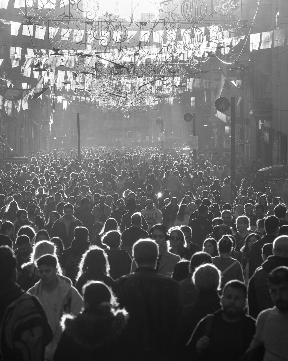 A dense crowd of people filling a street, backlit, receding into the distance